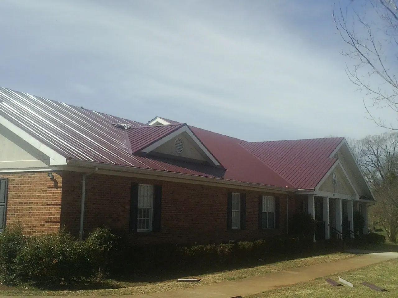Red metal roof with gabled entries on a long brick building, from a Hail Damage Roof Repair job in Cairo