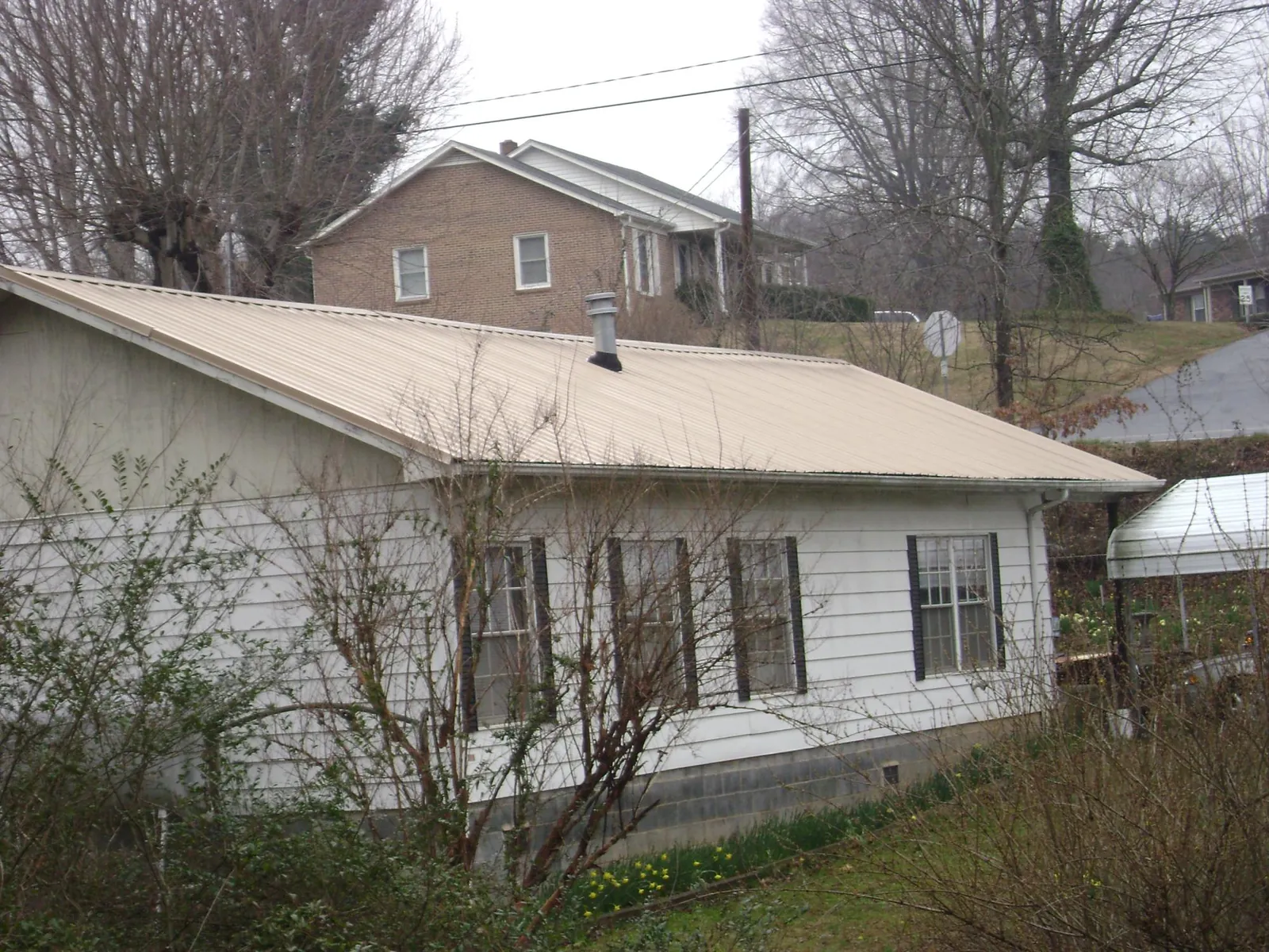 Tan metal roof on a white sided house set into a hillside — Commercial Roofing by Roofing Brothers in Cairo